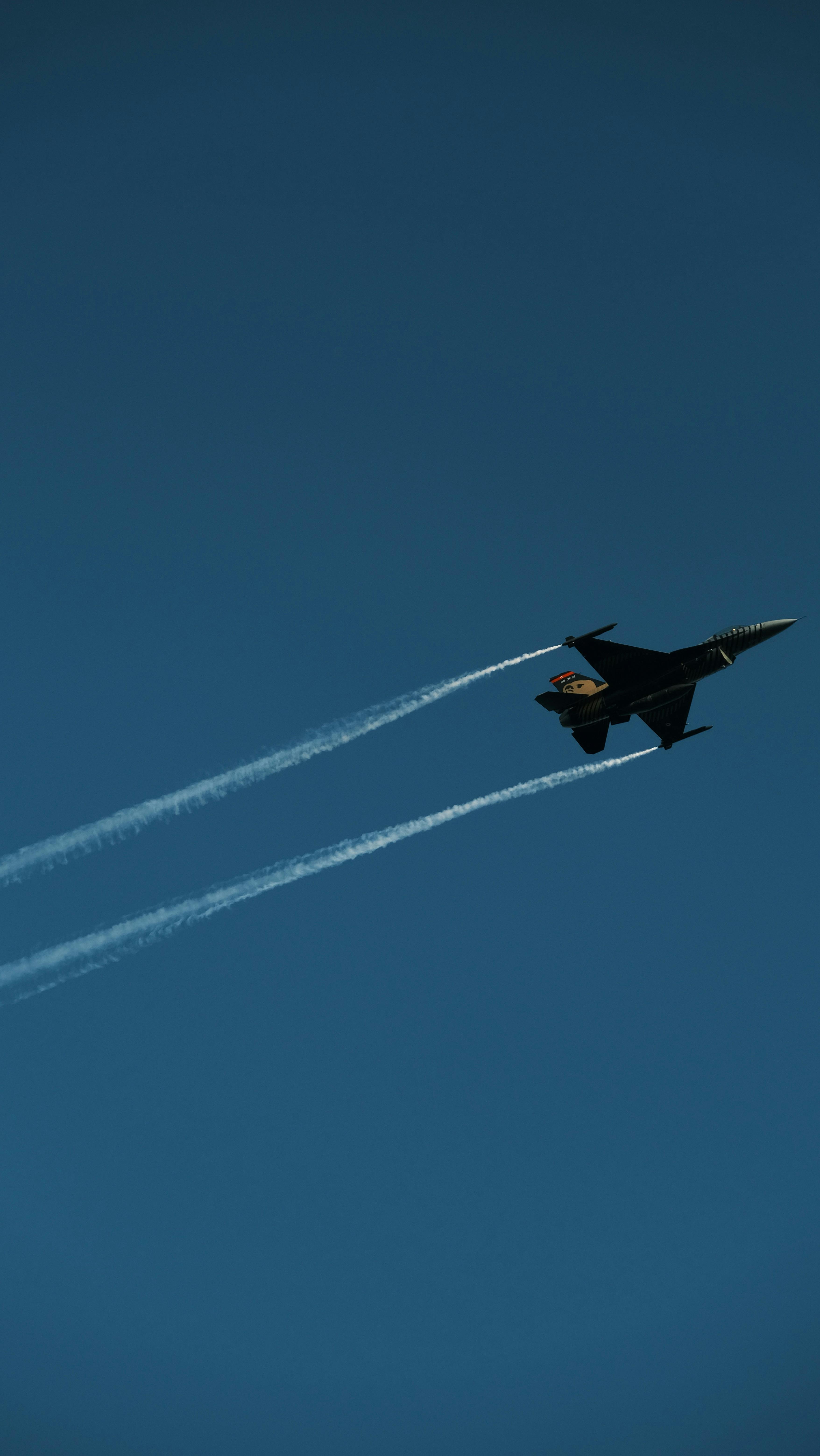 A fighter jet soars through the sky leaving contrasting contrails behind.