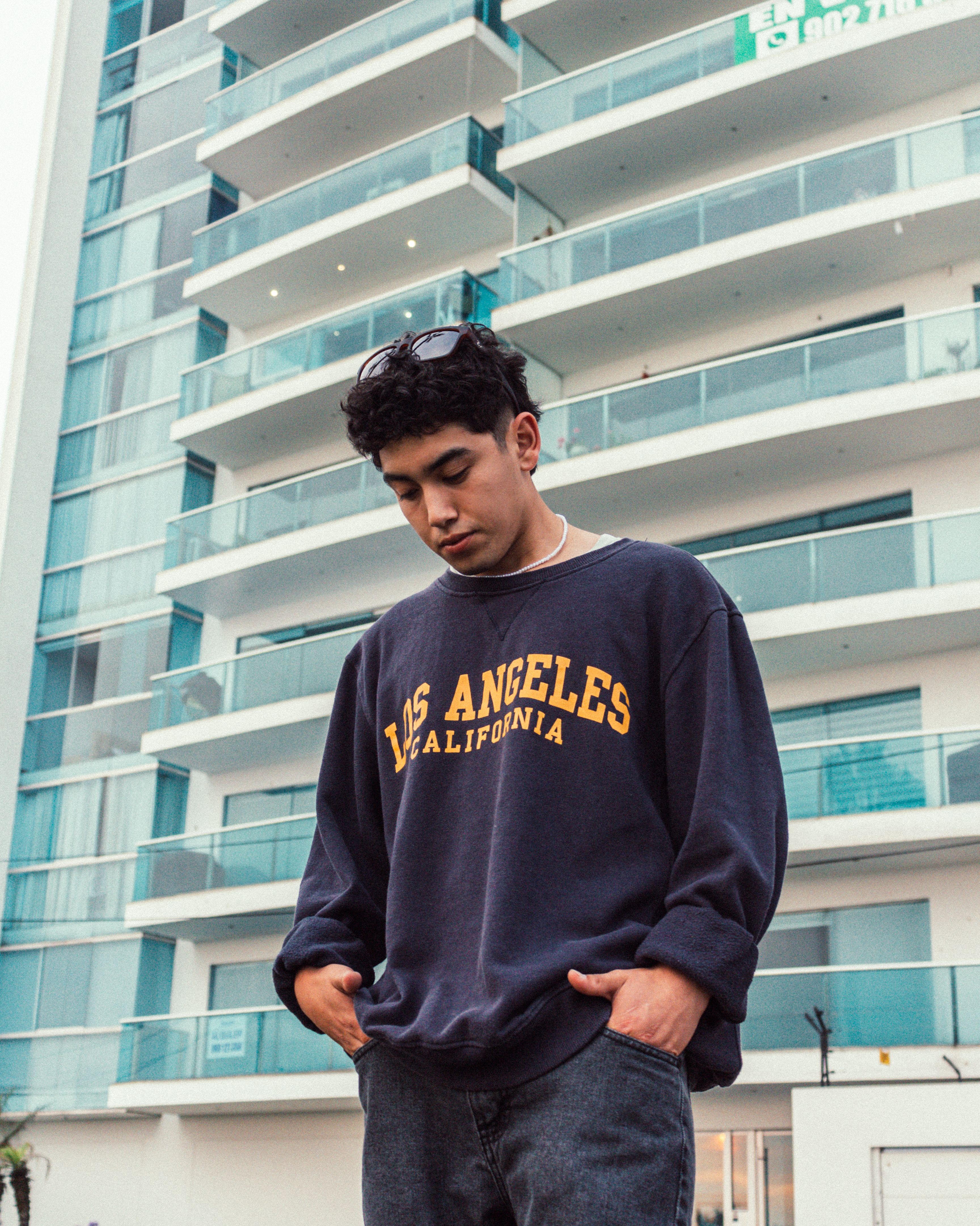 Young man in Los Angeles sweatshirt posing in front of modern building.