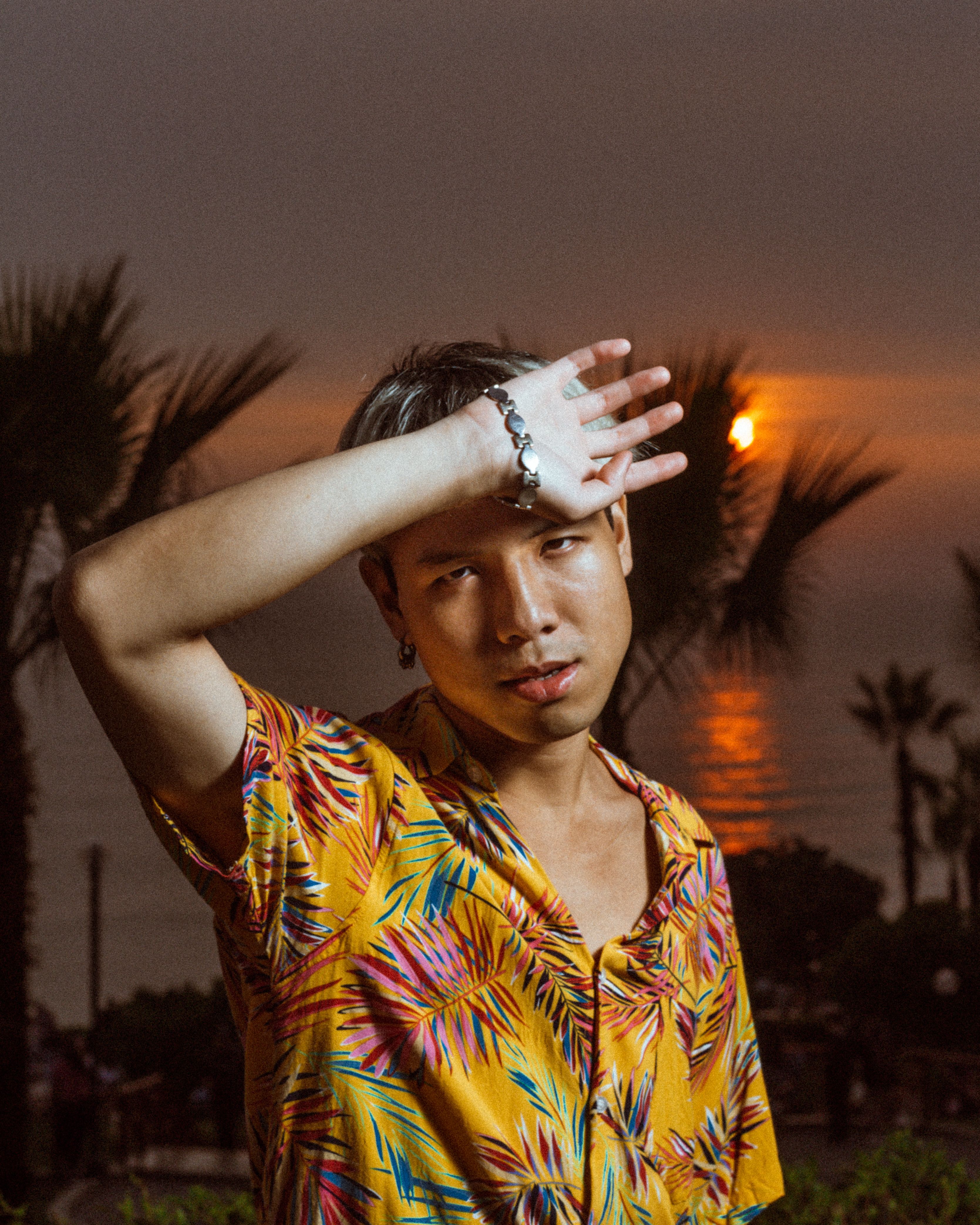 A person shielding eyes from the sun during a tropical beach sunset with palm trees.