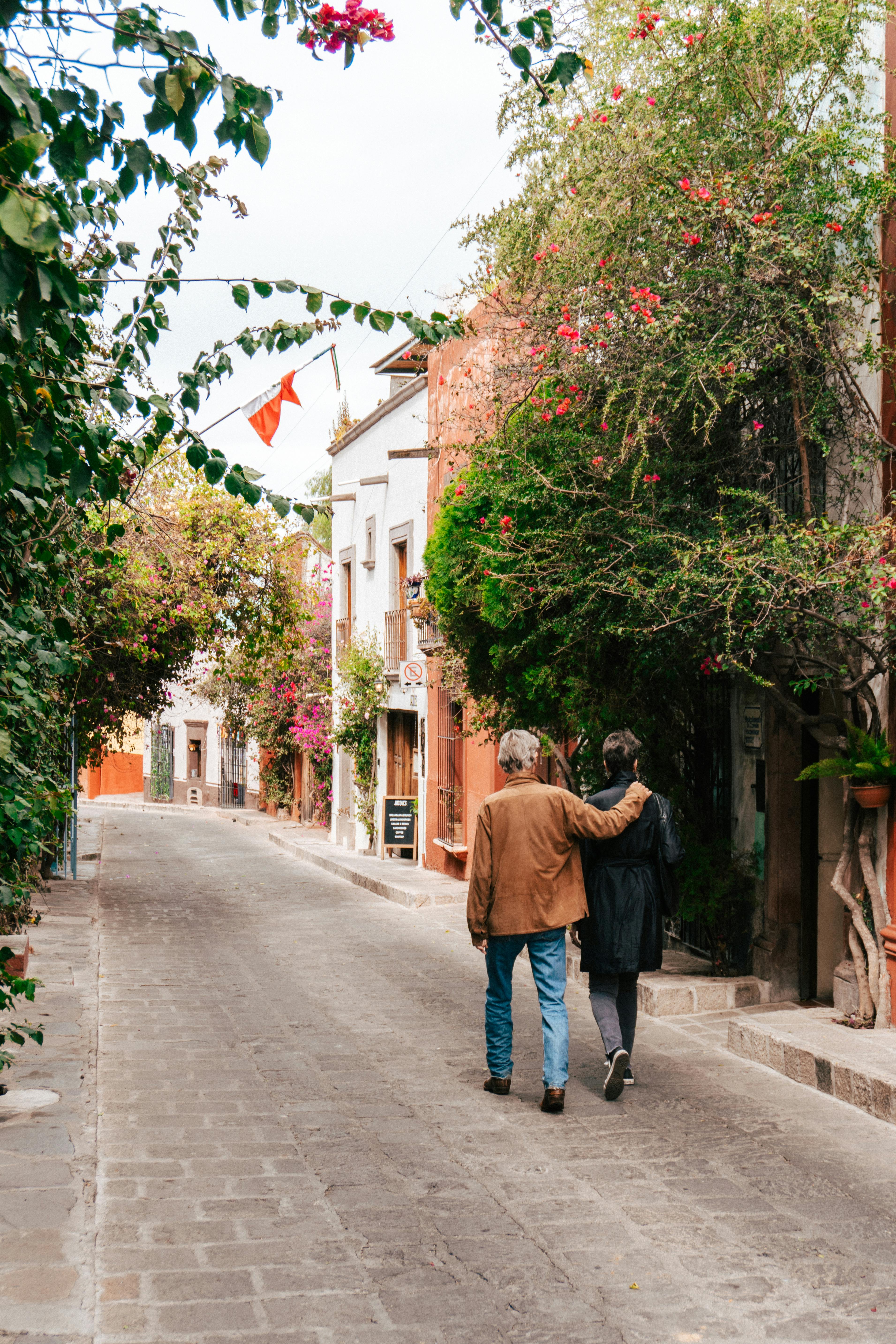 Two people walk down a picturesque street in Guanajuato, Mexico, surrounded by vibrant foliage.