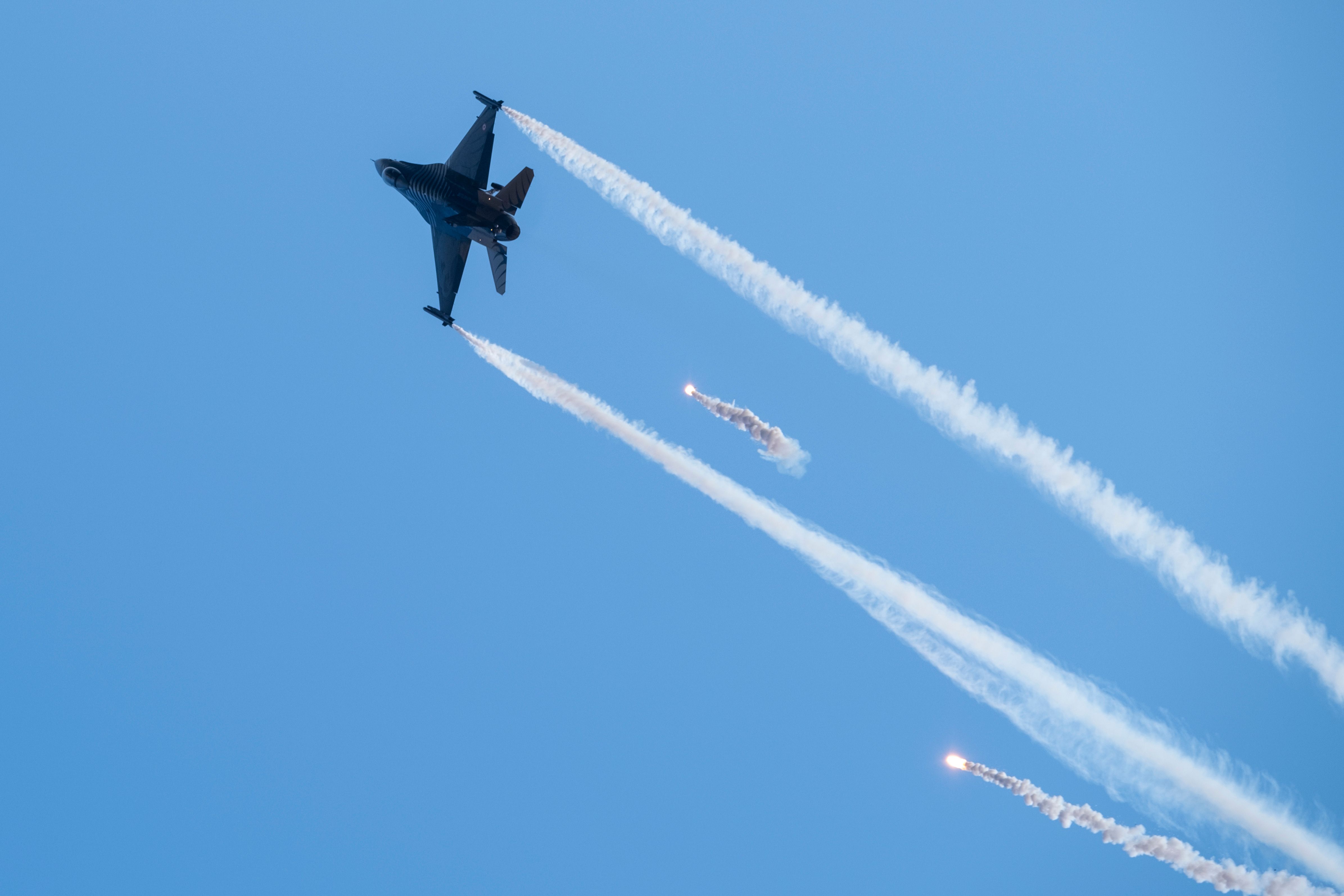 A fighter jet performing complex maneuvers with flare trails in a clear blue sky. (Photo by Soner Arkan on Pexels)