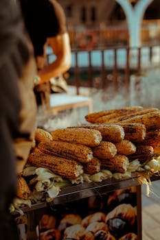 Grilled corn stacked at a street food stall during a vibrant sunset, capturing urban life.
