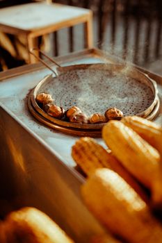 A close-up of corn and chestnuts roasting on a street vendor grill, creating a warm and rustic feel.