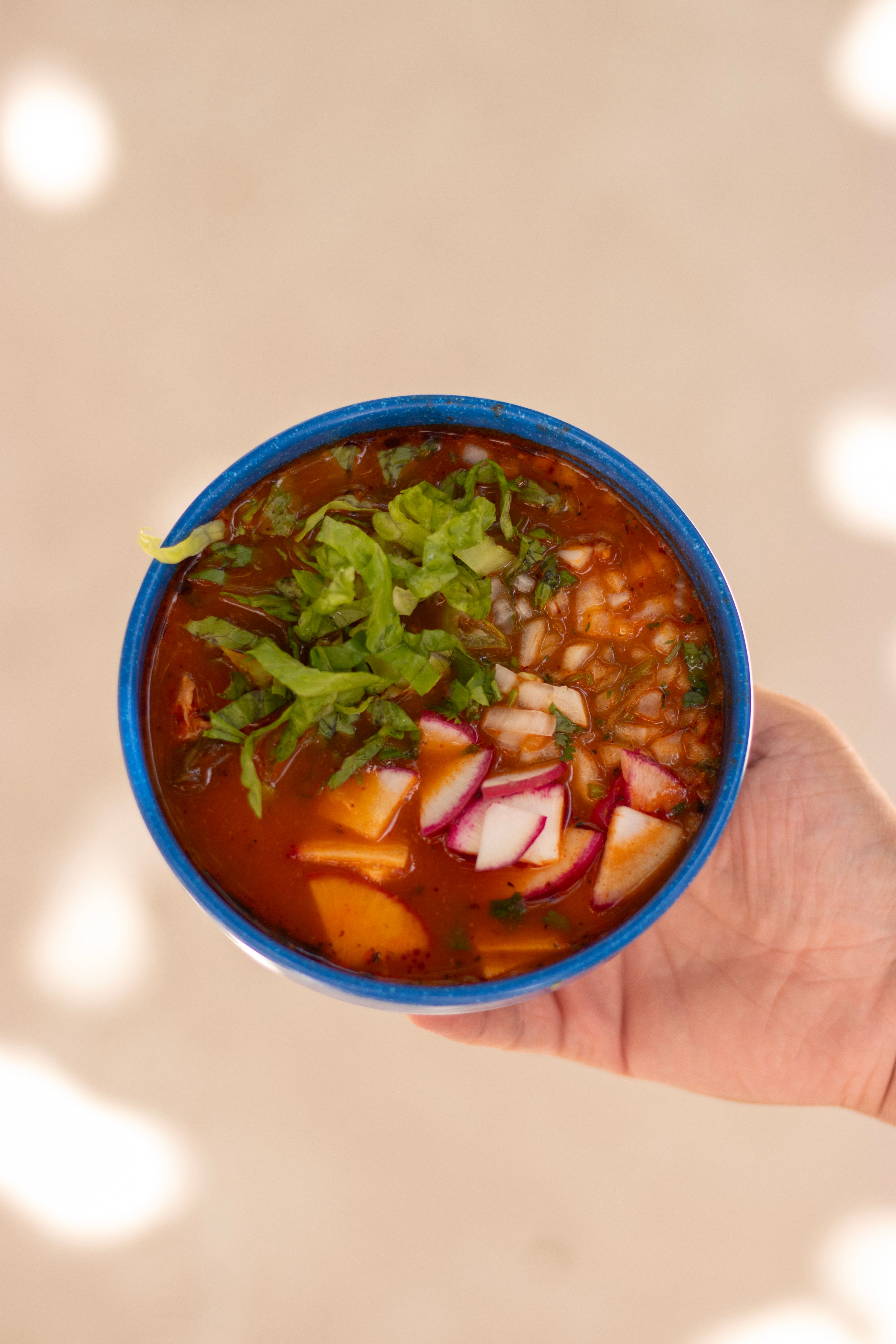 Close-up of a colorful Mexican pozole dish with fresh toppings in a blue bowl, showcasing traditional flavors.