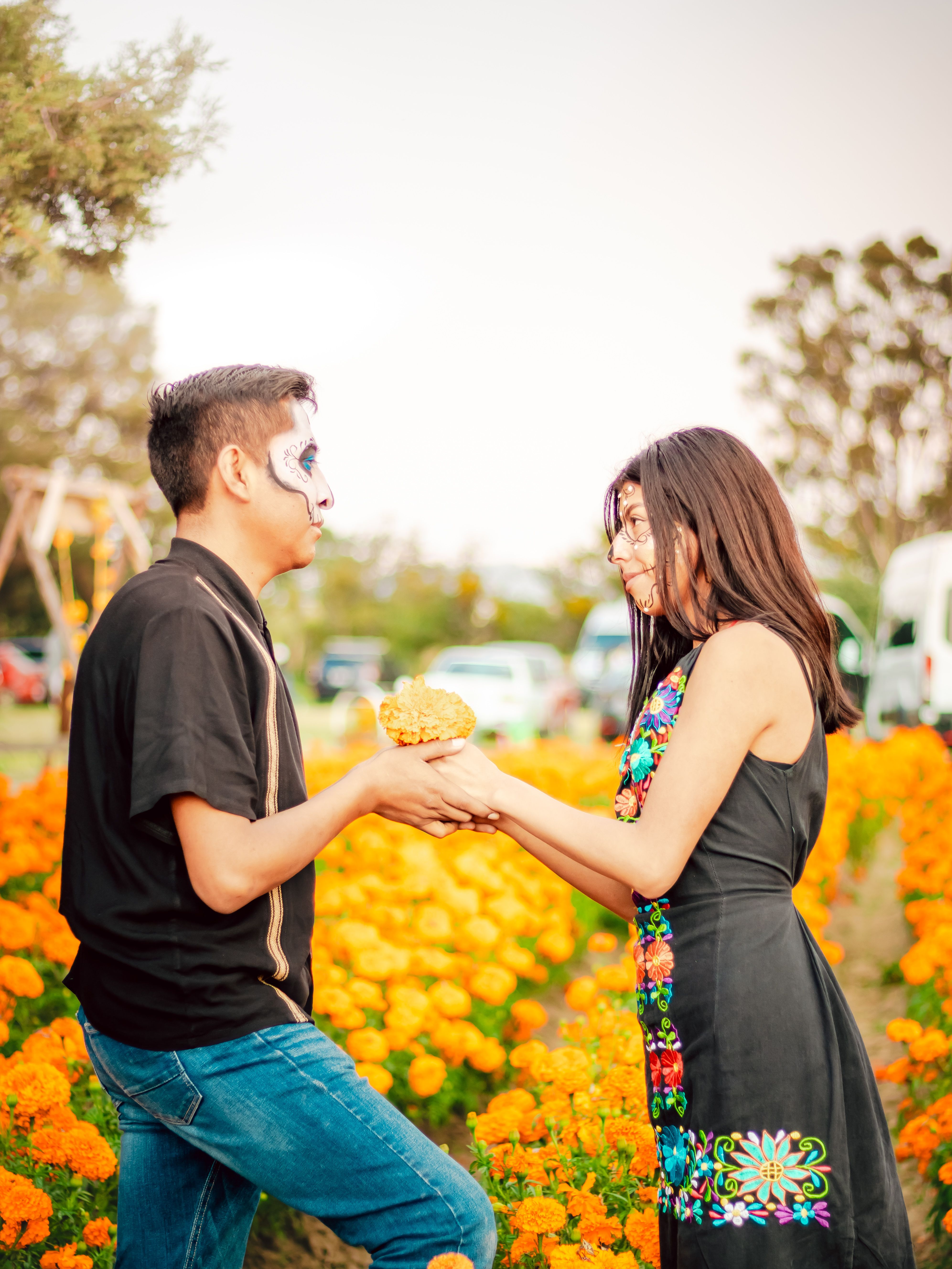 Couple with painted faces exchanging marigolds during Day of the Dead.