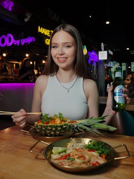 Smiling woman with Asian cuisine and beer bottle in lively restaurant setting.