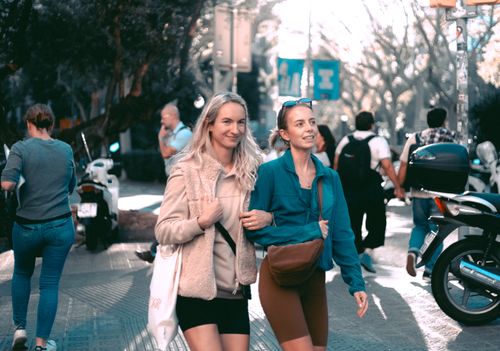 Free Two women enjoying a sunny day walking together on a busy urban street. Stock Photo