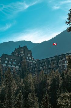 Majestic view of Fairmont Banff Springs Hotel with mountains and Canadian flag in the background.