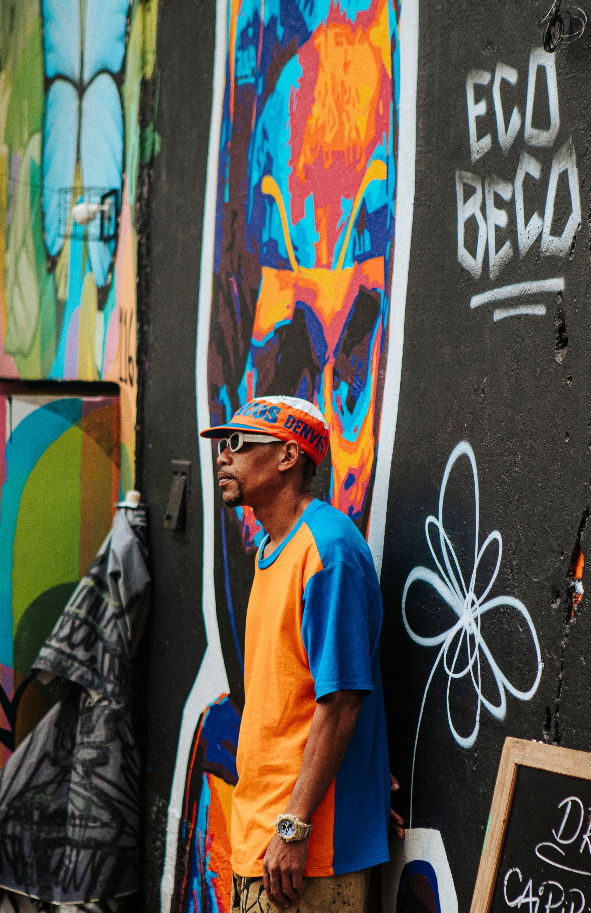 Man stands by vibrant street art mural and graffiti on city wall.