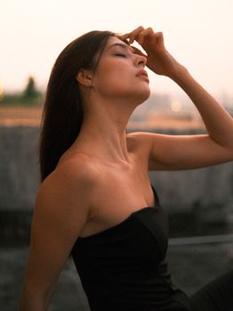 A stylish woman poses thoughtfully against a sunset backdrop, exuding elegance and contemplation.
