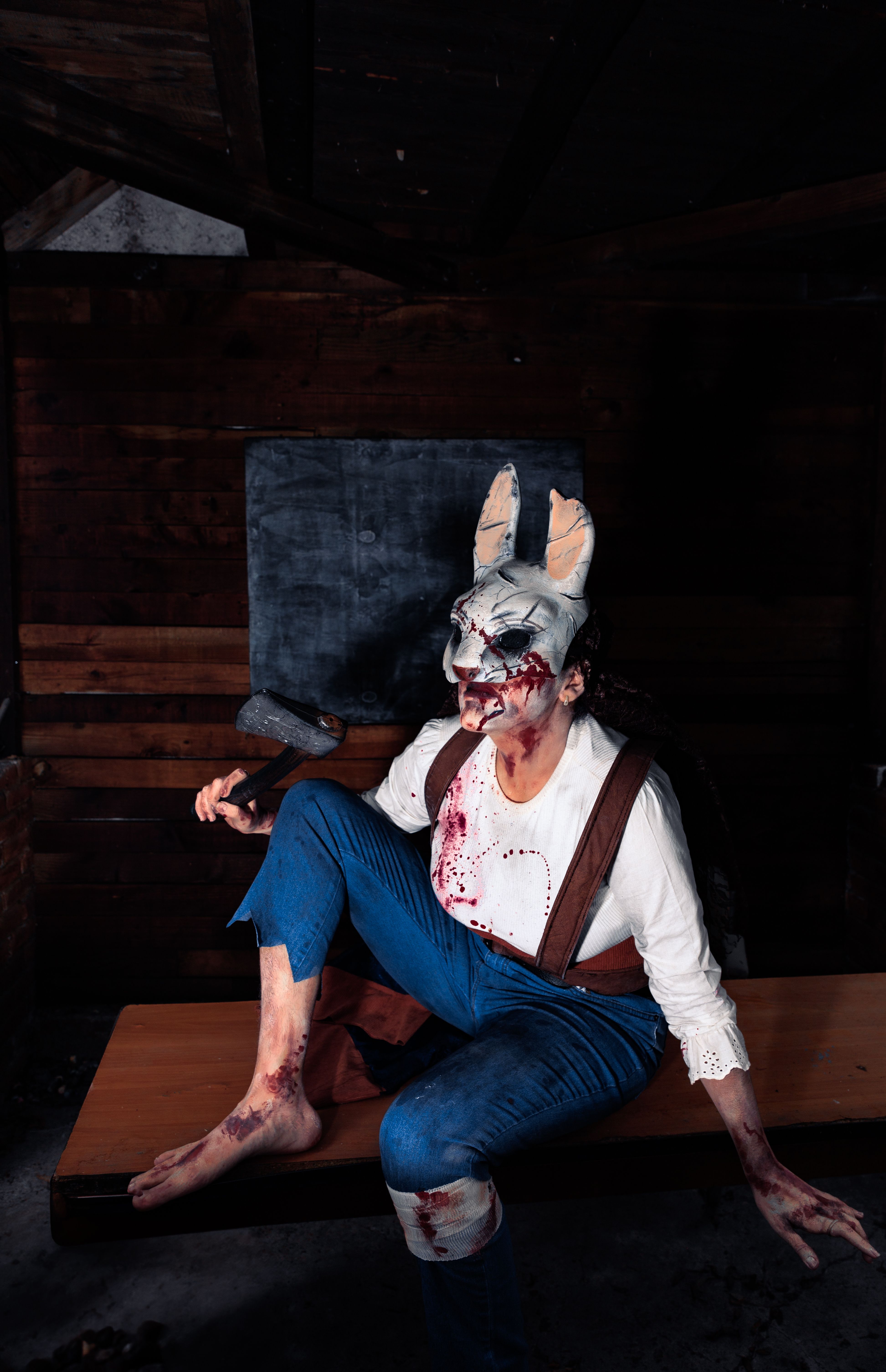 A person in a bloody rabbit costume holding a hammer sitting in a dark room.