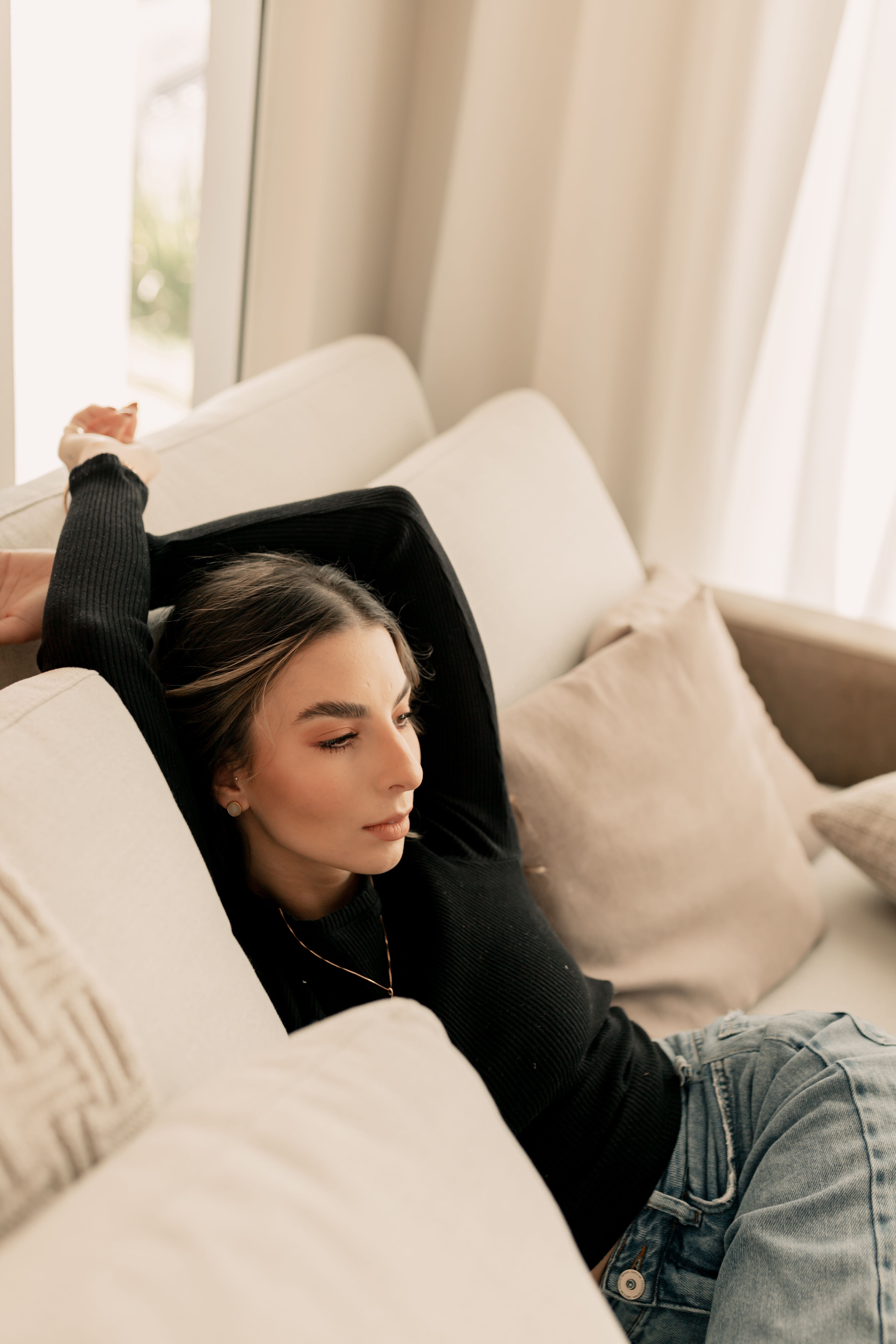 Fotomural Una mujer se relaja en un sofá en una habitación acogedora y bien iluminada, vestida con jeans casuales y un suéter de punto.