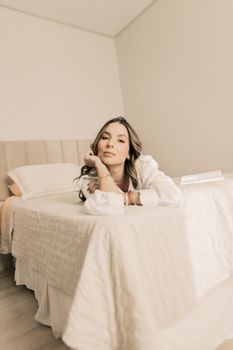 A young woman in a relaxed pose on a bed in a minimalist bedroom setting.
