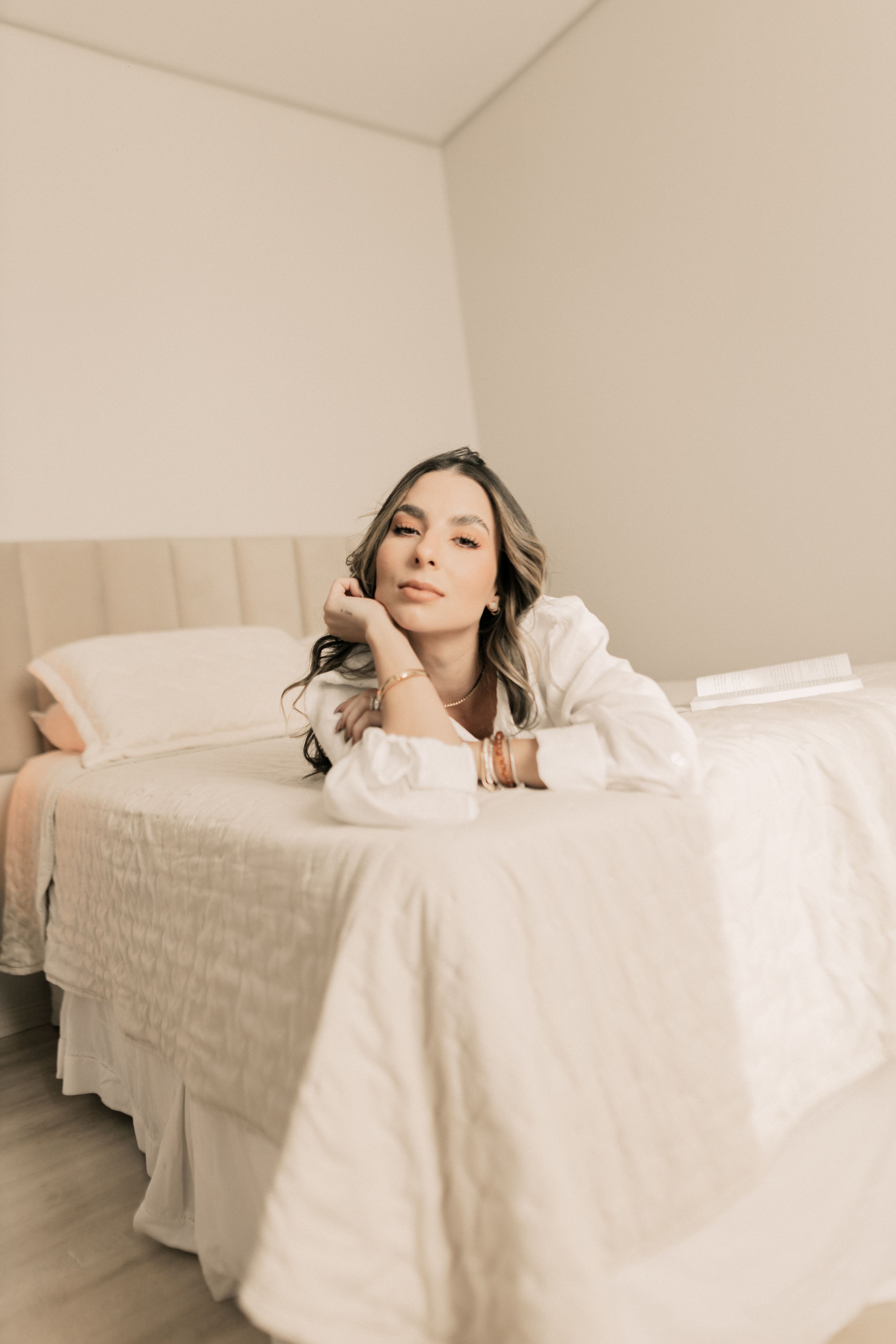 Uma mulher jovem em uma pose relaxada em uma cama em um ambiente de quarto minimalista.
