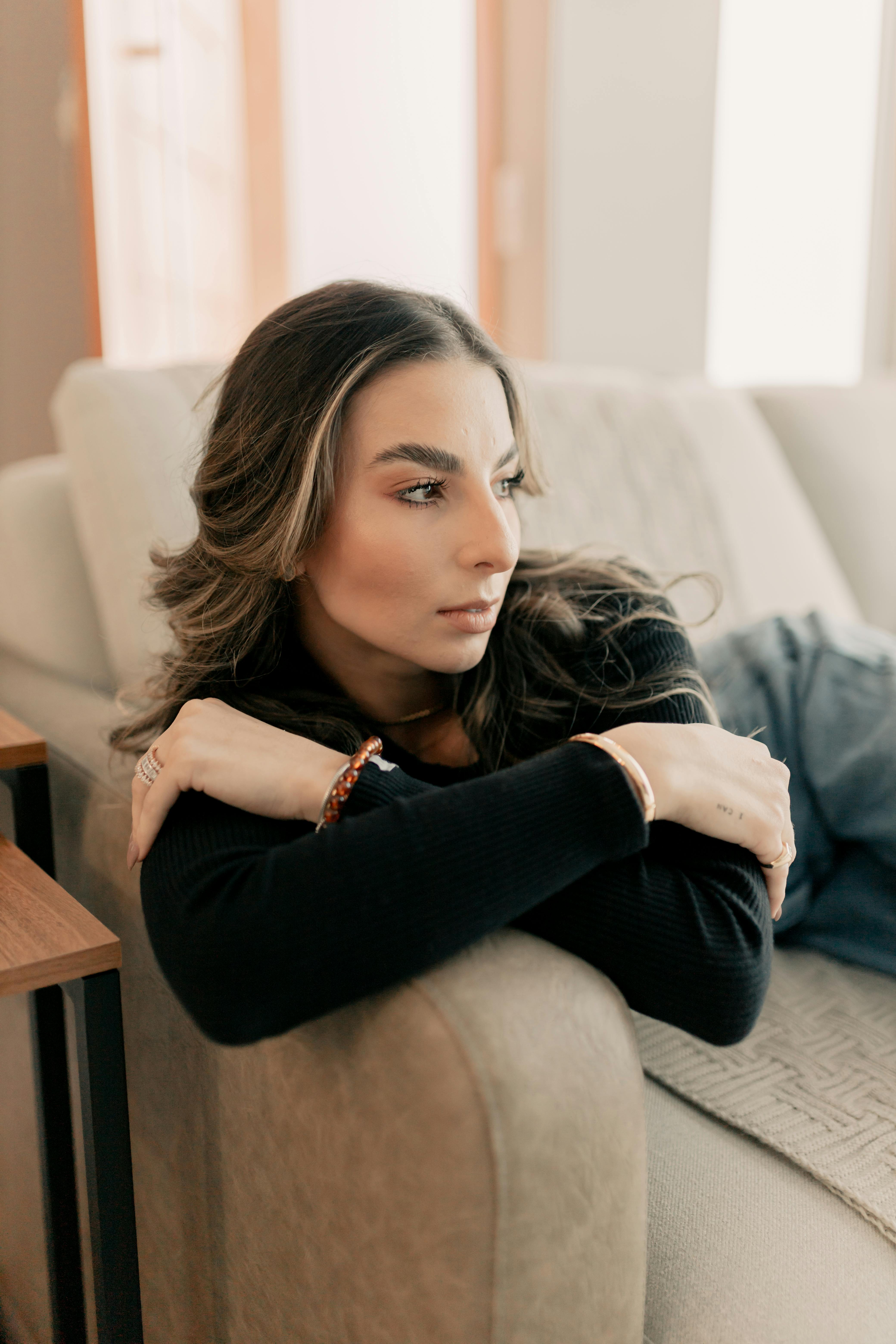 Young woman in black sweater relaxing on a couch, looking thoughtful.