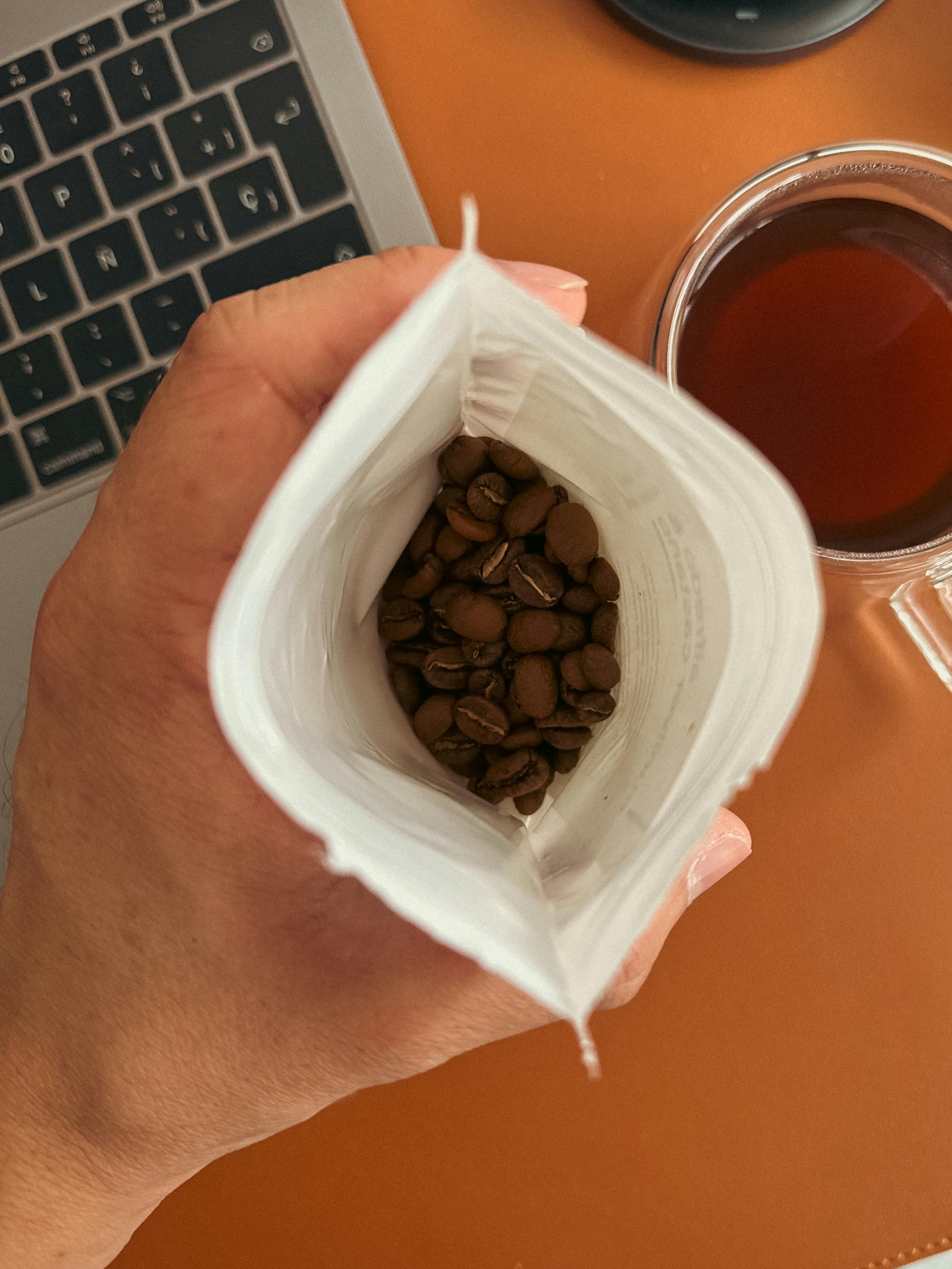 Fresh coffee beans in a white bag with a laptop and coffee cup nearby, perfect for work-from-home concept.