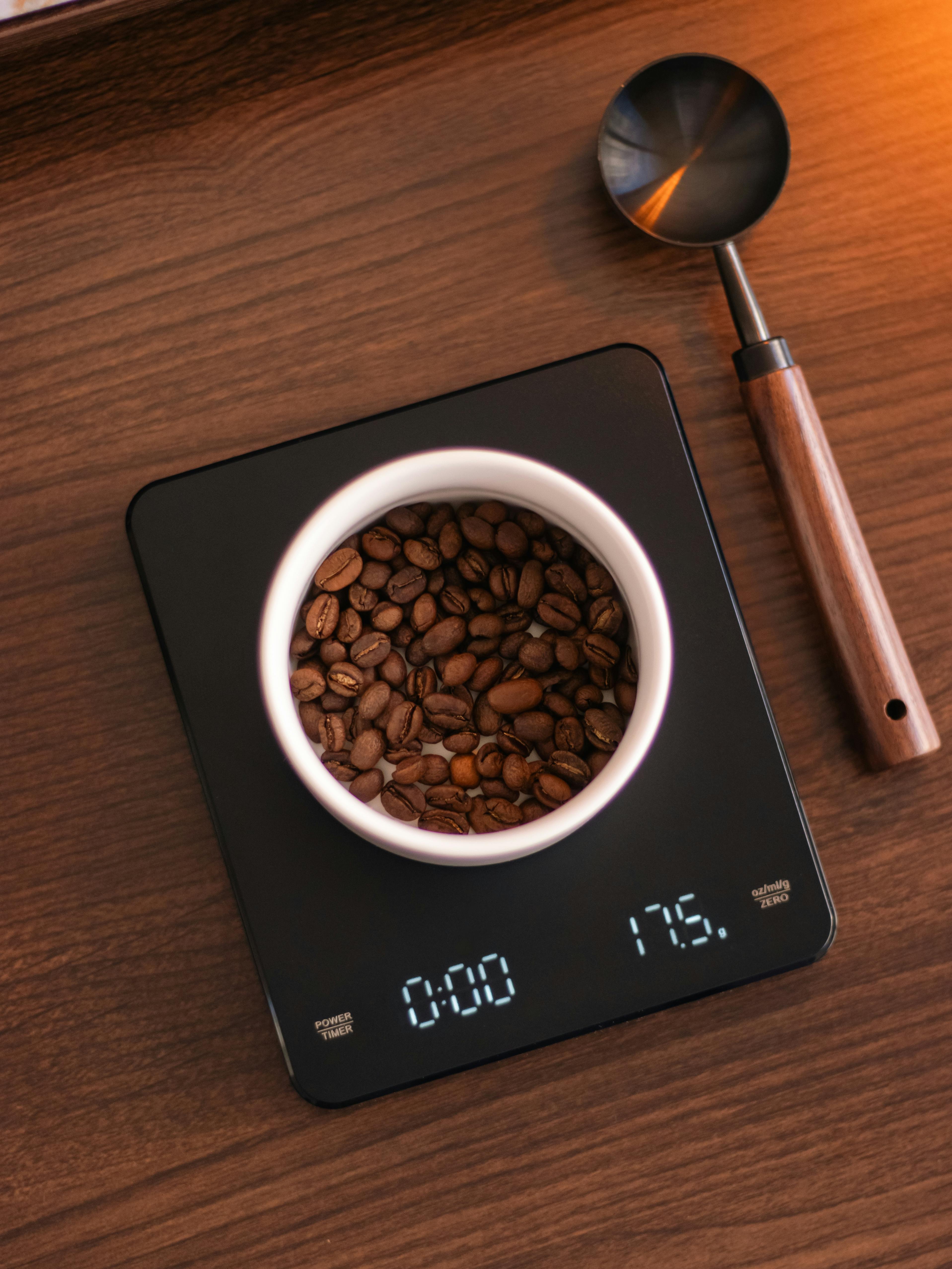 Free Close-up of coffee beans on a digital scale with a wooden scoop in warm natural light. Stock Photo