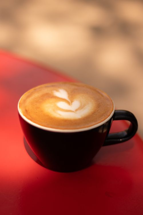 Free Close-up of a beautifully prepared latte in a black cup on a vibrant red table. Stock Photo
