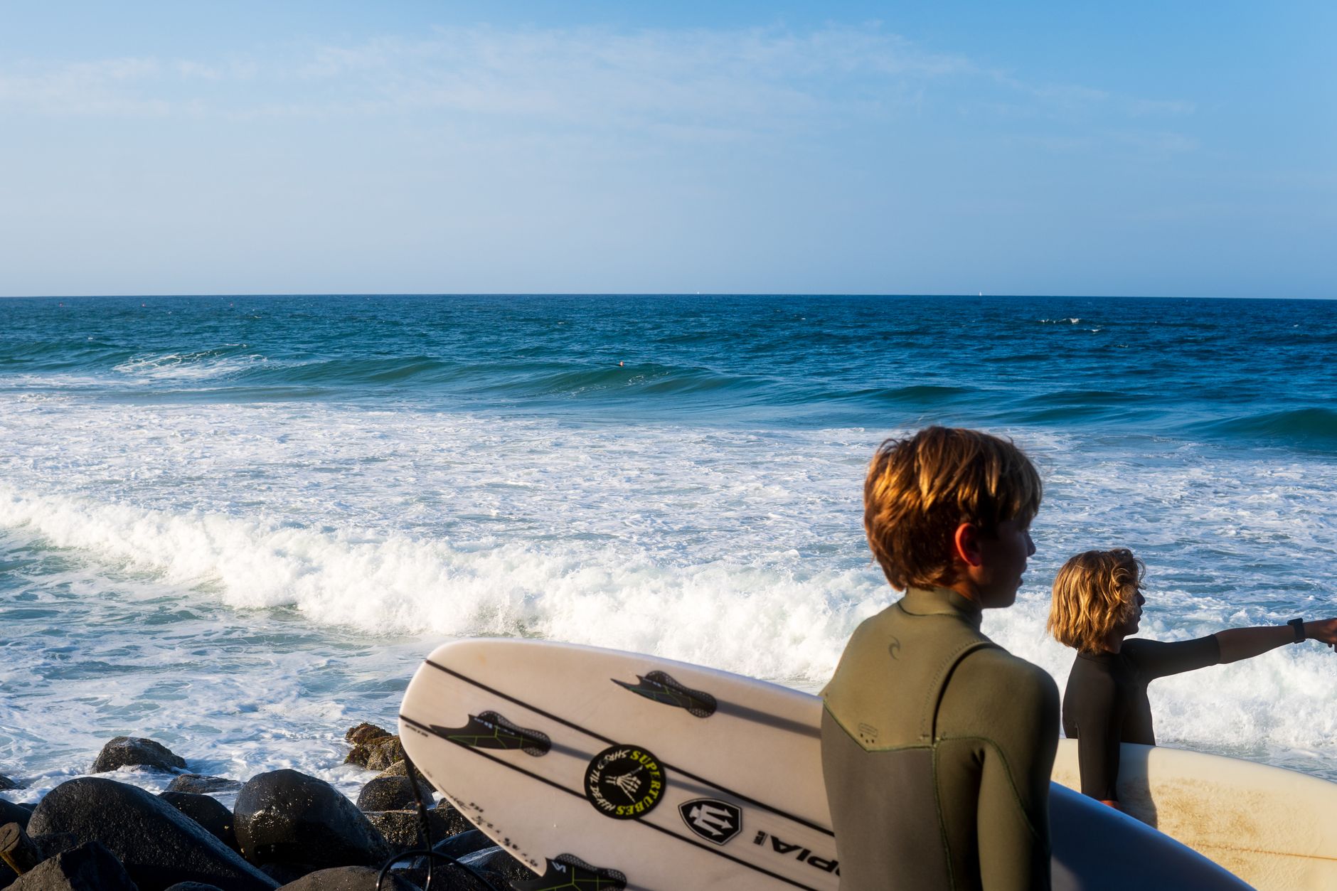 Two young surfers prepare to hit the waves on a sunny beach day. Ideal for ocean and adventure themes.