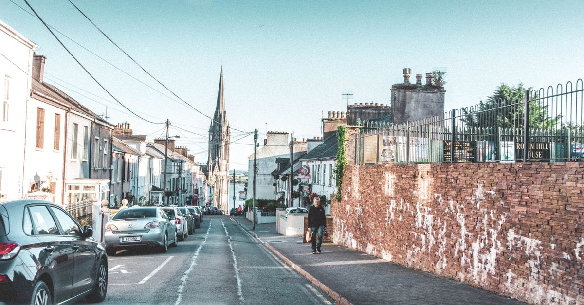 A picturesque street view in Ireland, showcasing cars, old buildings, and a church spire.