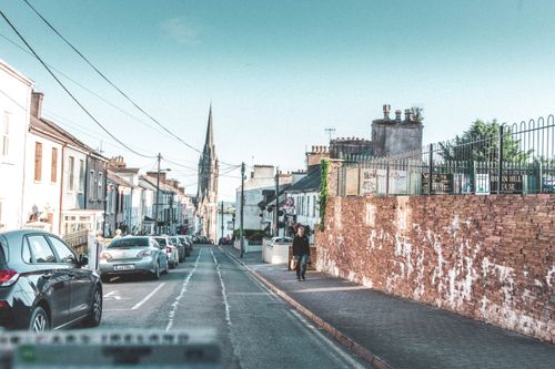 Free A picturesque street view in Ireland, showcasing cars, old buildings, and a church spire. Stock Photo