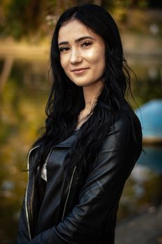 Captivating portrait of a young woman in a leather jacket with natural outdoor background.