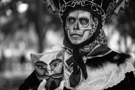 Catrina in traditional makeup and costume holding a mask for Day of the Dead in Mexico City.
