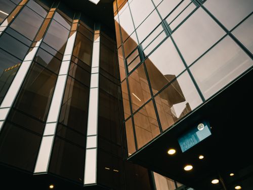 Free Upward view of a modern glass building facade reflecting the sky and surroundings. Stock Photo
