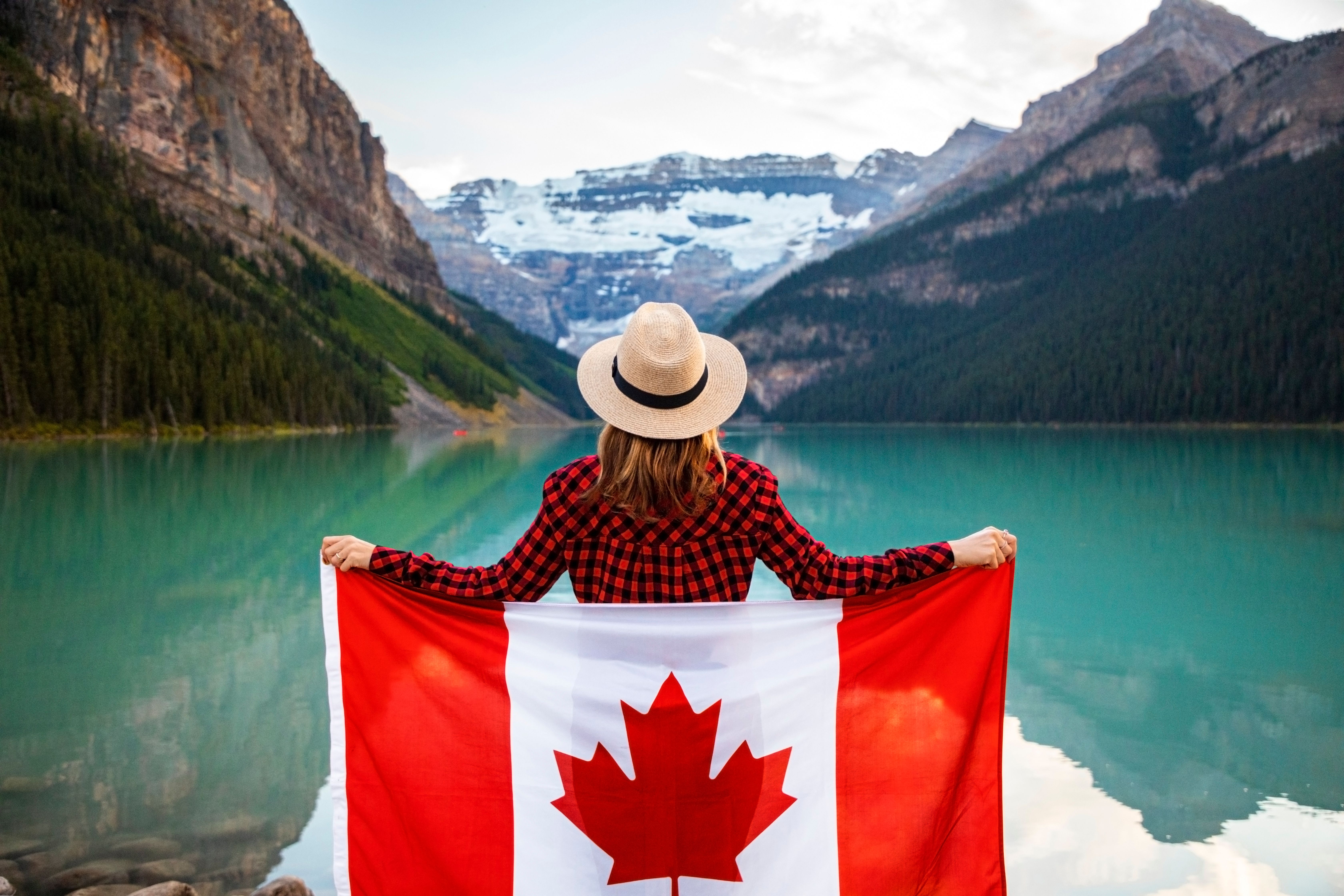 Person holding a Canadian flag overlooking a mountain lake, symbolizing life and career opportunities in Canada