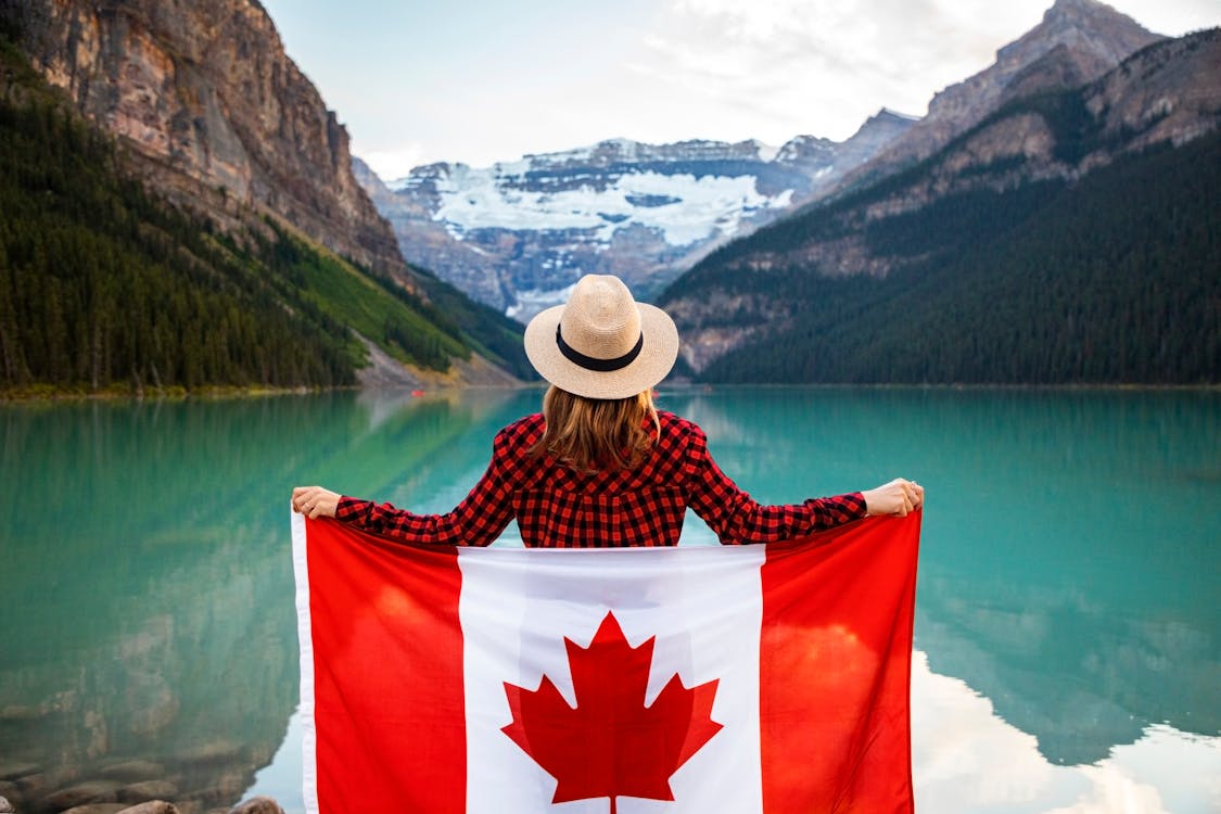 女人穿著紅色和黑色格仔的恤衫和米色軟呢帽拿著加拿大國旗看著湖