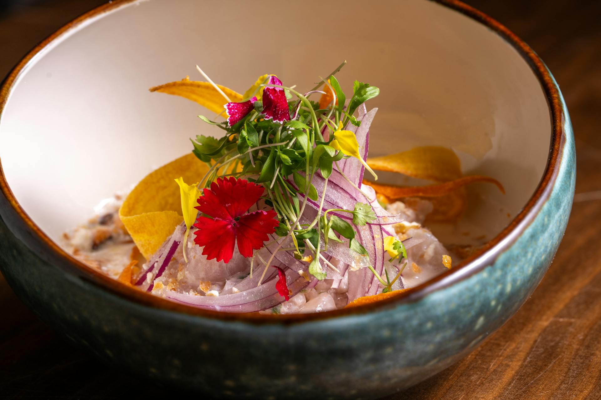 A vibrant dish of ceviche topped with colorful microgreens and edible flowers in a rustic bowl.