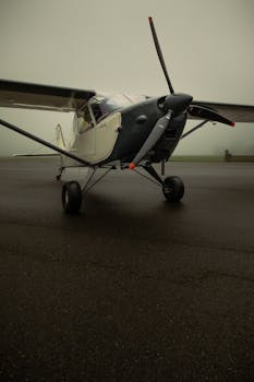 Close-up of a small propeller airplane on a foggy runway, ready for takeoff.