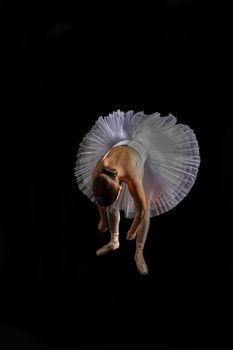 Ballet dancer in a graceful pose wearing a white tutu on a black background.