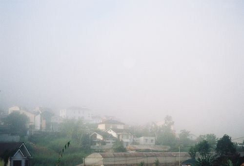 Free A serene village scene with houses enveloped in dense fog on a misty morning. Stock Photo