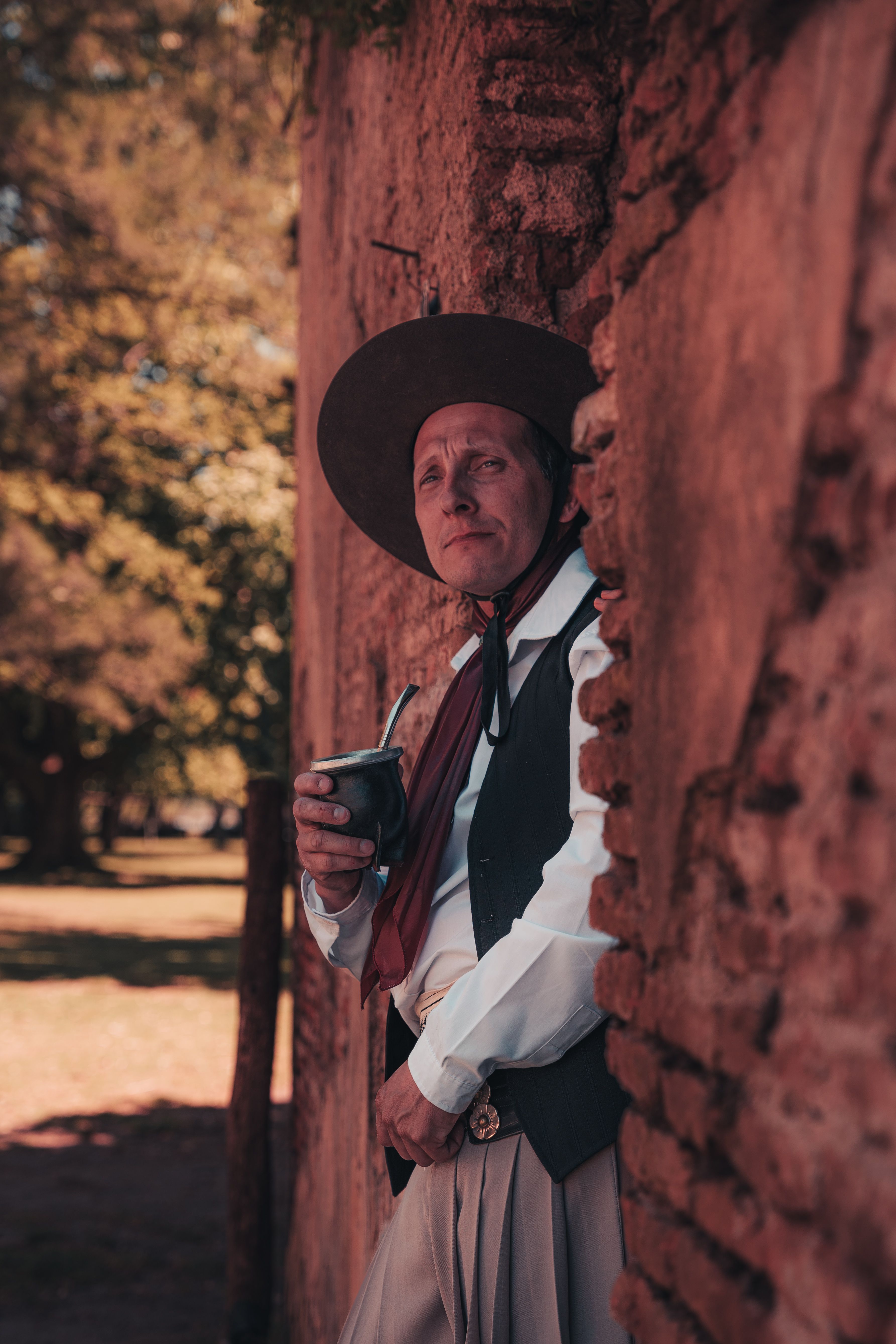 A gaucho in traditional attire leaning against a rustic wall outdoors.
