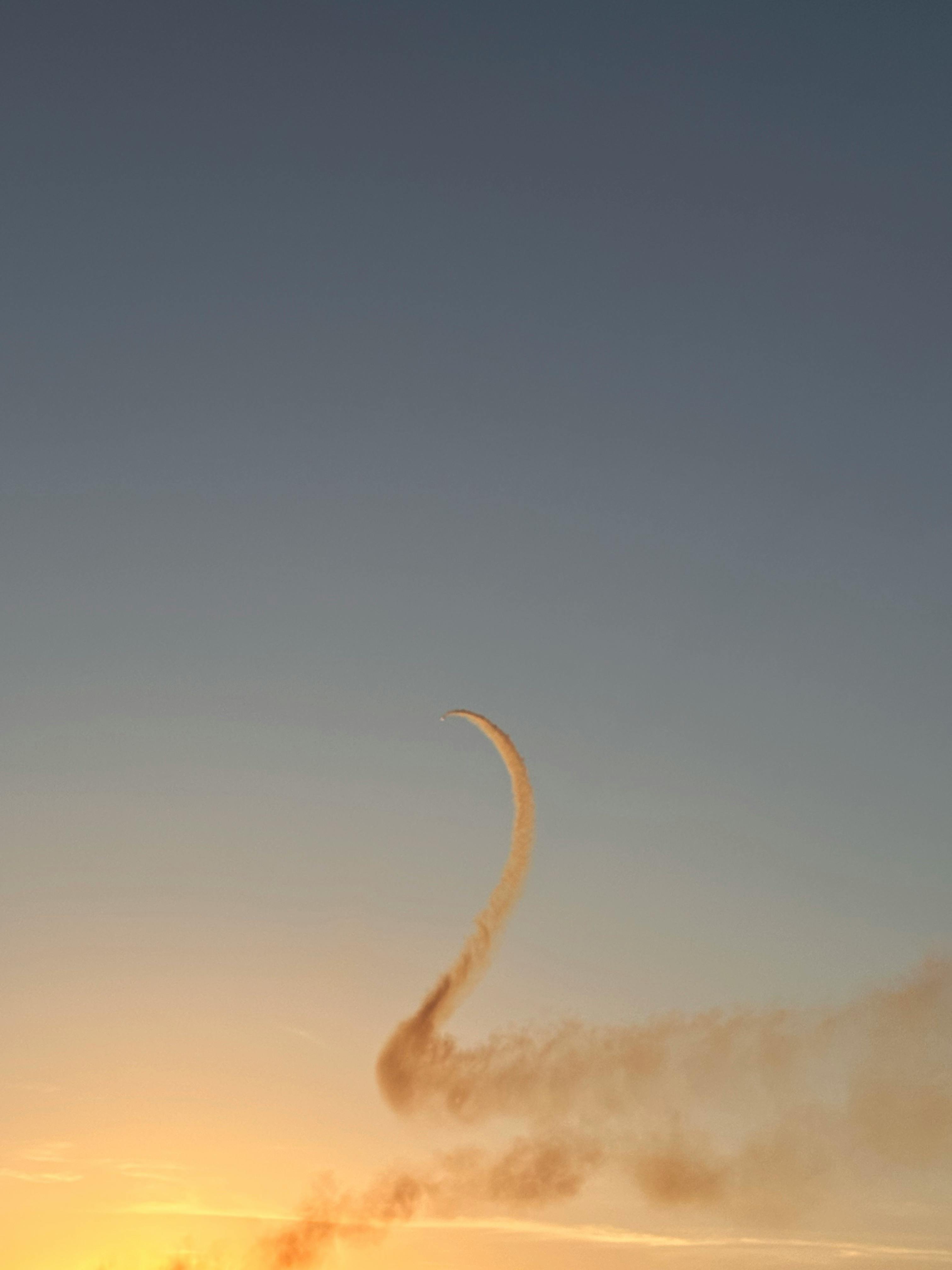 A jet's elegant smoke trail curves against a vibrant İzmir sunset sky.