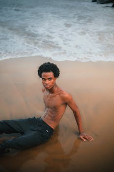 Young man relaxing on a sandy beach with waves in Abuja, Nigeria.