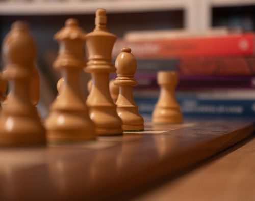 Free Focus on wooden chess pieces lined up on a chessboard with books in the background. Stock Photo