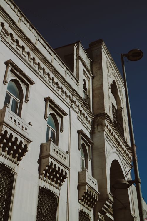 Free Close-up of a historic building facade with ornate arched windows under a clear blue sky. Stock Photo