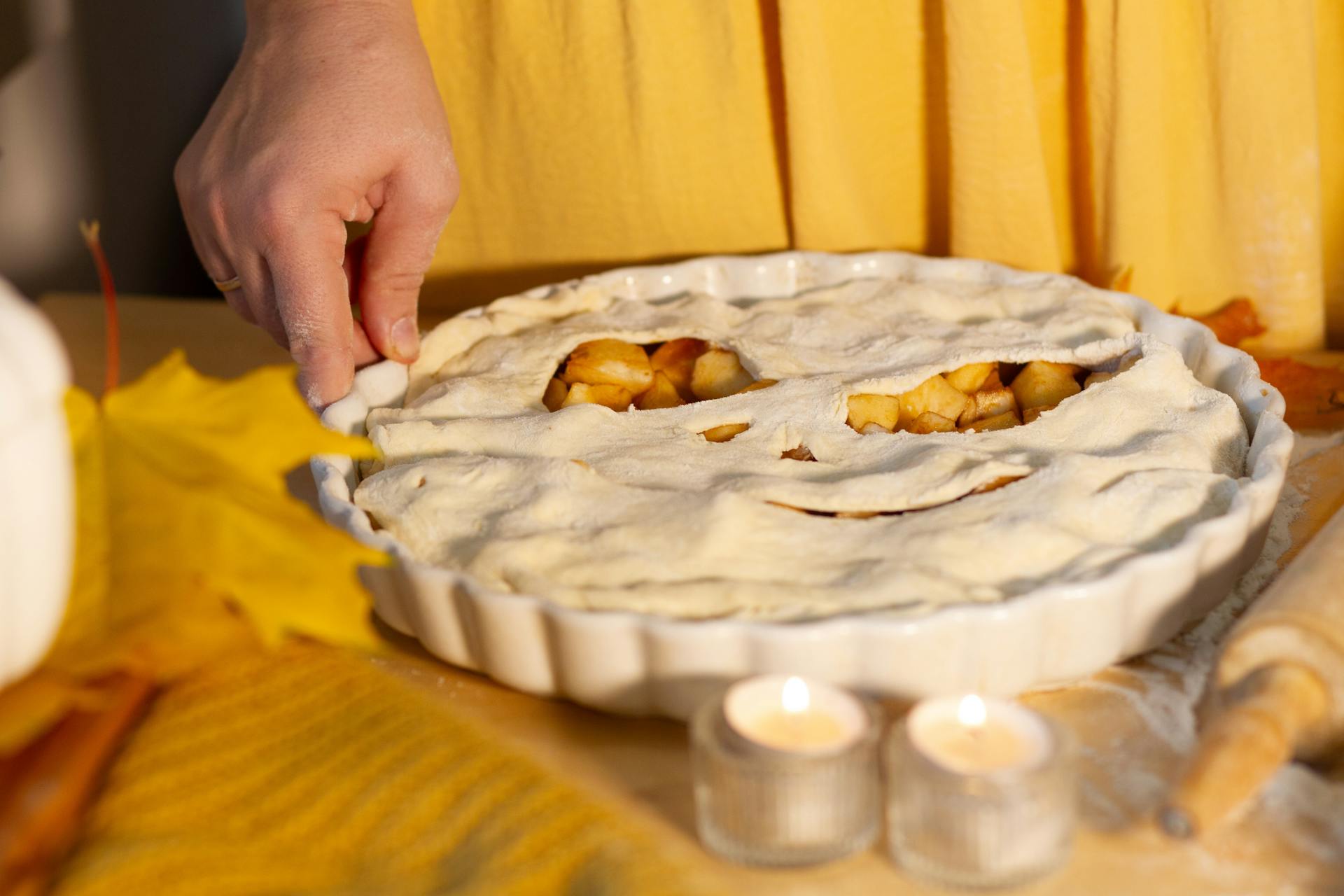 Hand preparing apple pie with homemade crust in cozy kitchen setting.