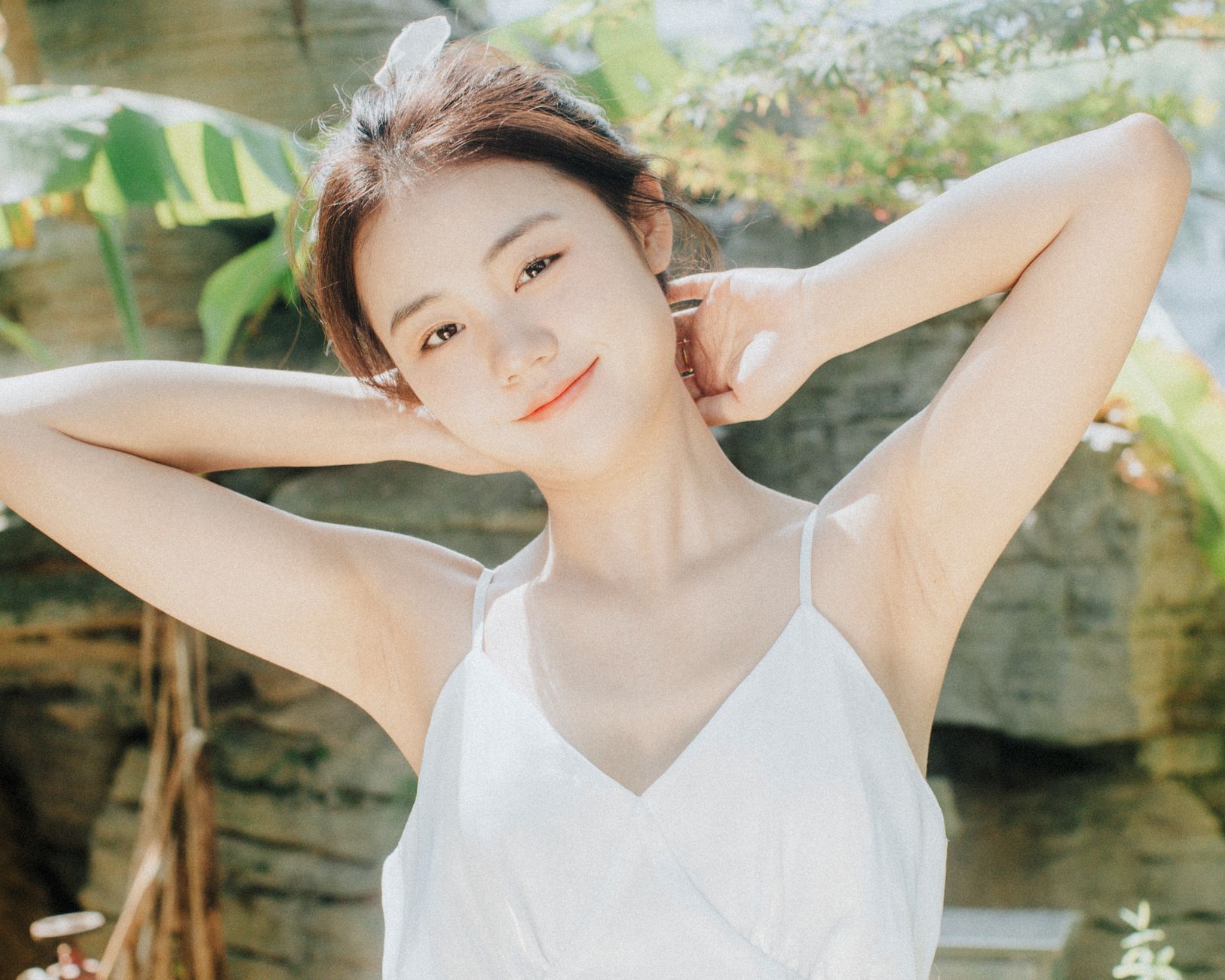 A young woman in a white dress enjoying the sunlight outdoors with a joyful expression.