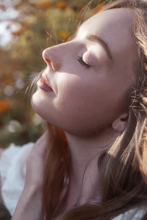 Free Close-up portrait of a young woman with eyes closed, basking in sunlight, outdoors. Stock Photo