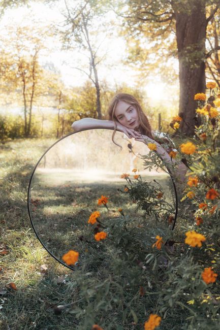Dreamy portrait of a woman with mirror reflection amidst autumn foliage and marigold flowers.