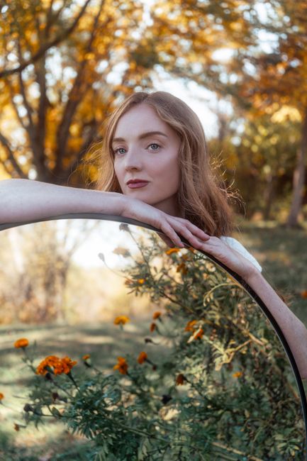 A serene portrait of a woman using a mirror artfully reflecting autumn foliage.