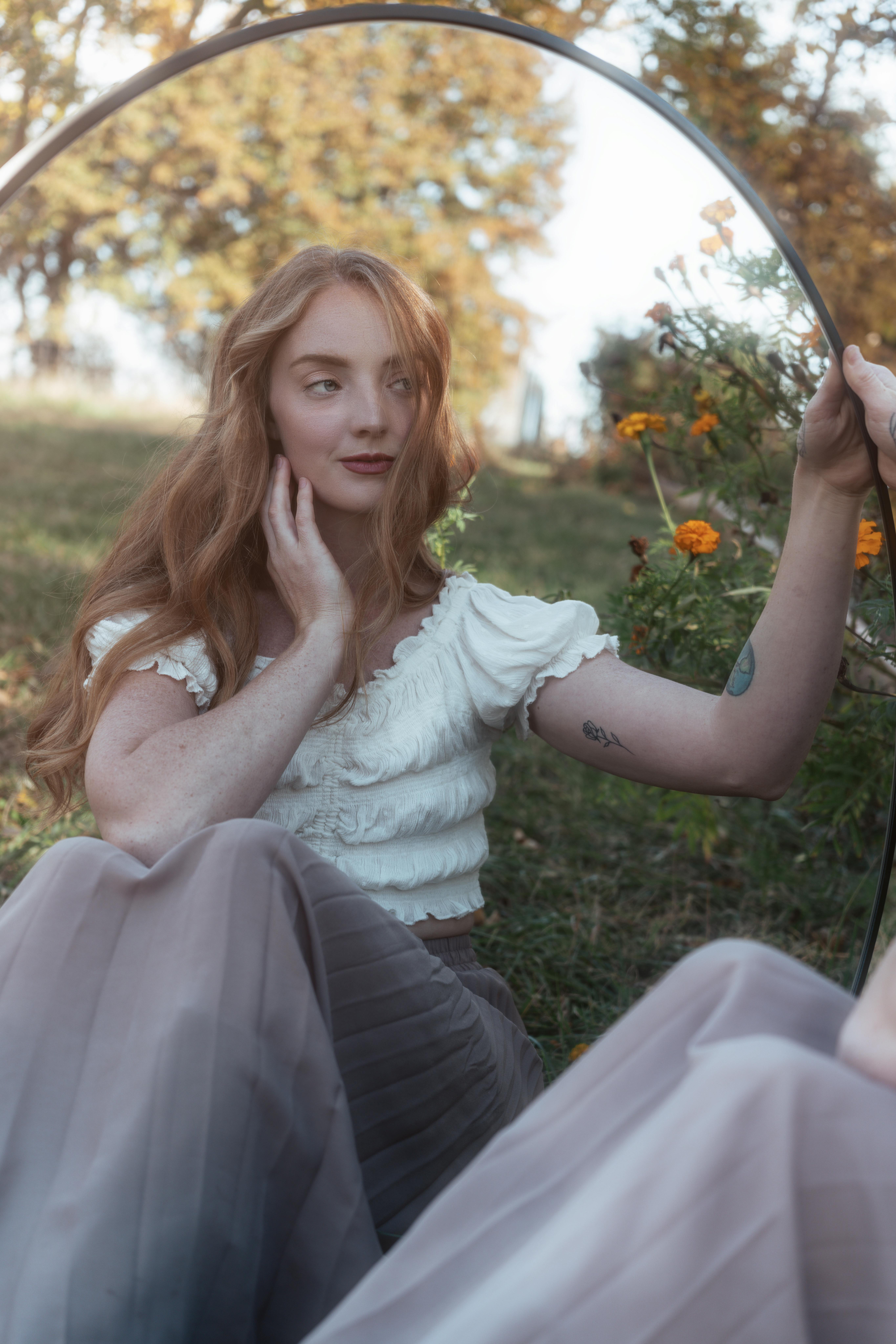 A serene outdoor portrait capturing a pensive woman with red hair using mirror reflections.