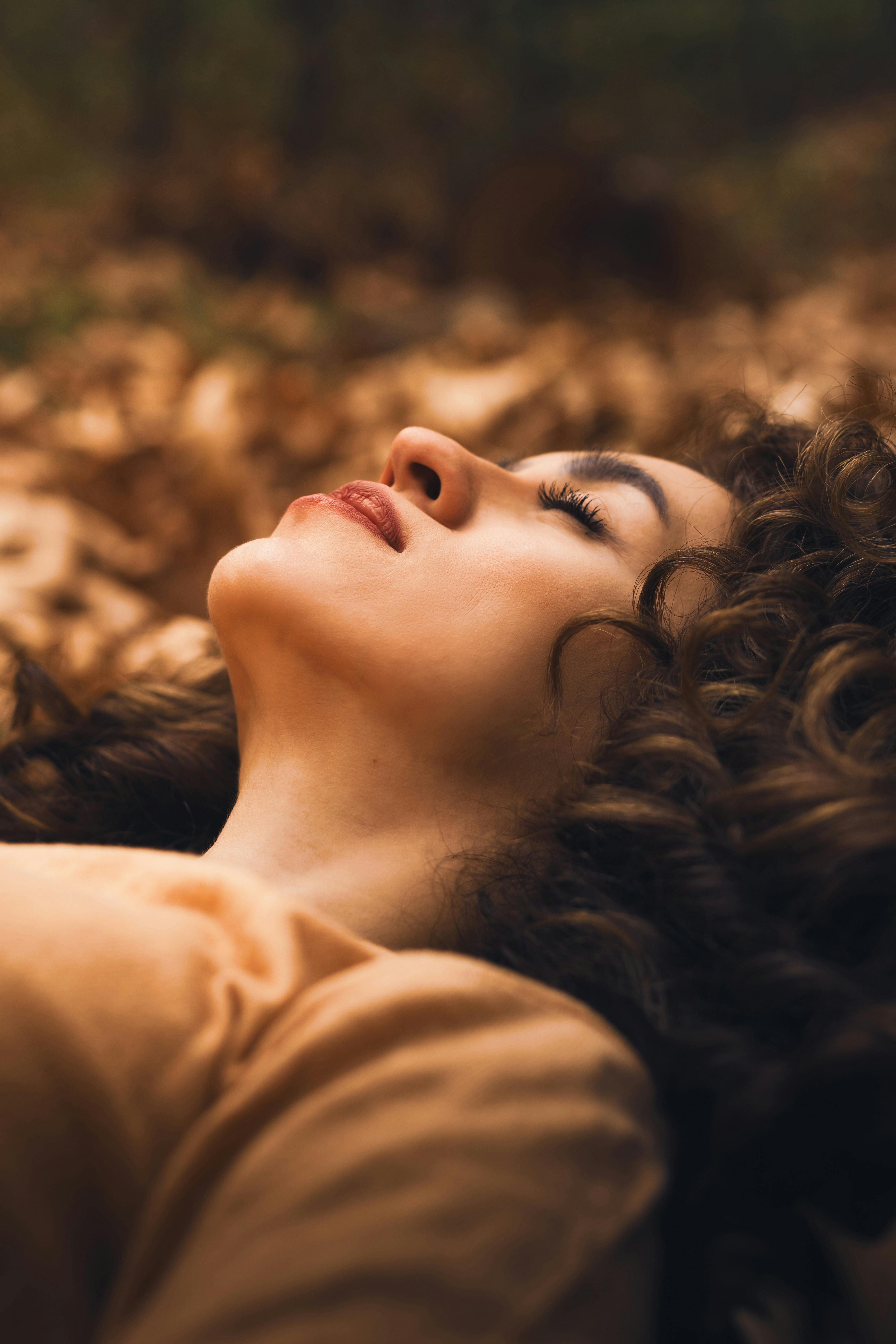 Relaxed woman lying peacefully on autumn leaves outdoors, eyes closed in complete calm and dreamy afterglow