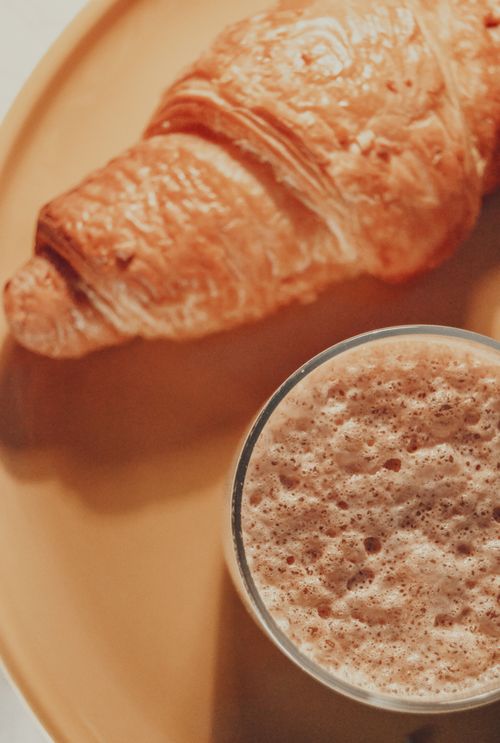 Free Golden brown croissant served with a frothy coffee, perfect breakfast combo. Stock Photo