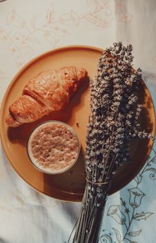 A warm and inviting breakfast scene featuring a croissant and coffee with lavender.