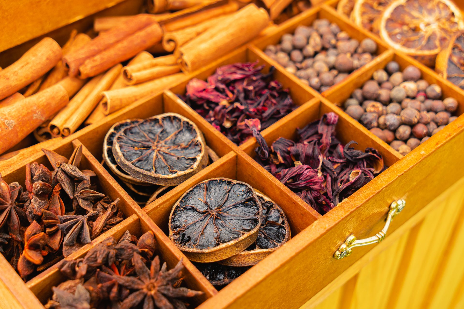 Top view of assorted dried spices and herbs in a wooden box, featuring anise, cinnamon, and dried citrus slices.