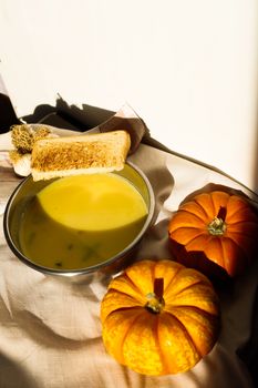 Warm pumpkin soup served with bread and two pumpkins, perfect for a cozy fall meal.